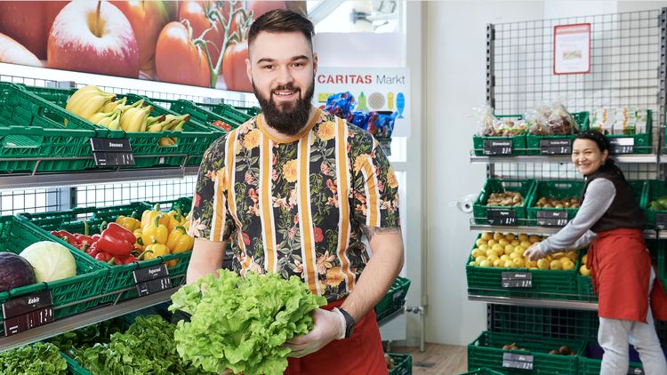 Ein Verkäufer im Caritas-Laden mit einem Salat in der Hand