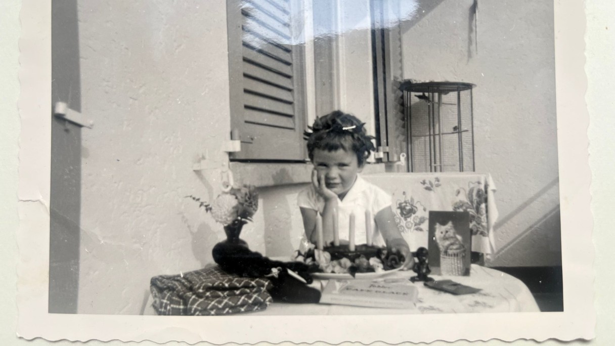 Auf einem schwarzweiss Foto ist ein vierjähriges Mädchen vor dem Geburtstagskuchen zu sehen.