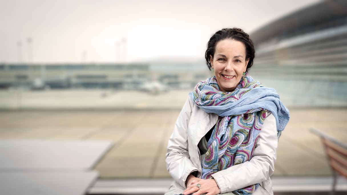 Andrea Thali lächelt in die Kamera, im Hintergrund ist der Flughafen zu sehen